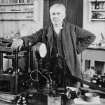 Thomas Edison standing next to equipment on work bench