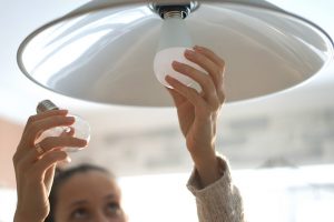 Woman changing light bulb in overhead light to energy efficient bulb